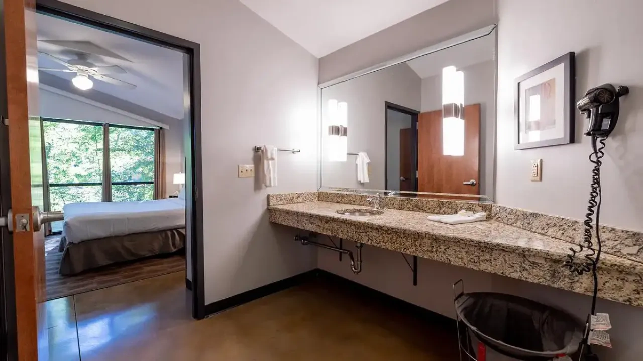 Hotel room bathroom with granite sink, large mirror, and view into bedroom with a bed.