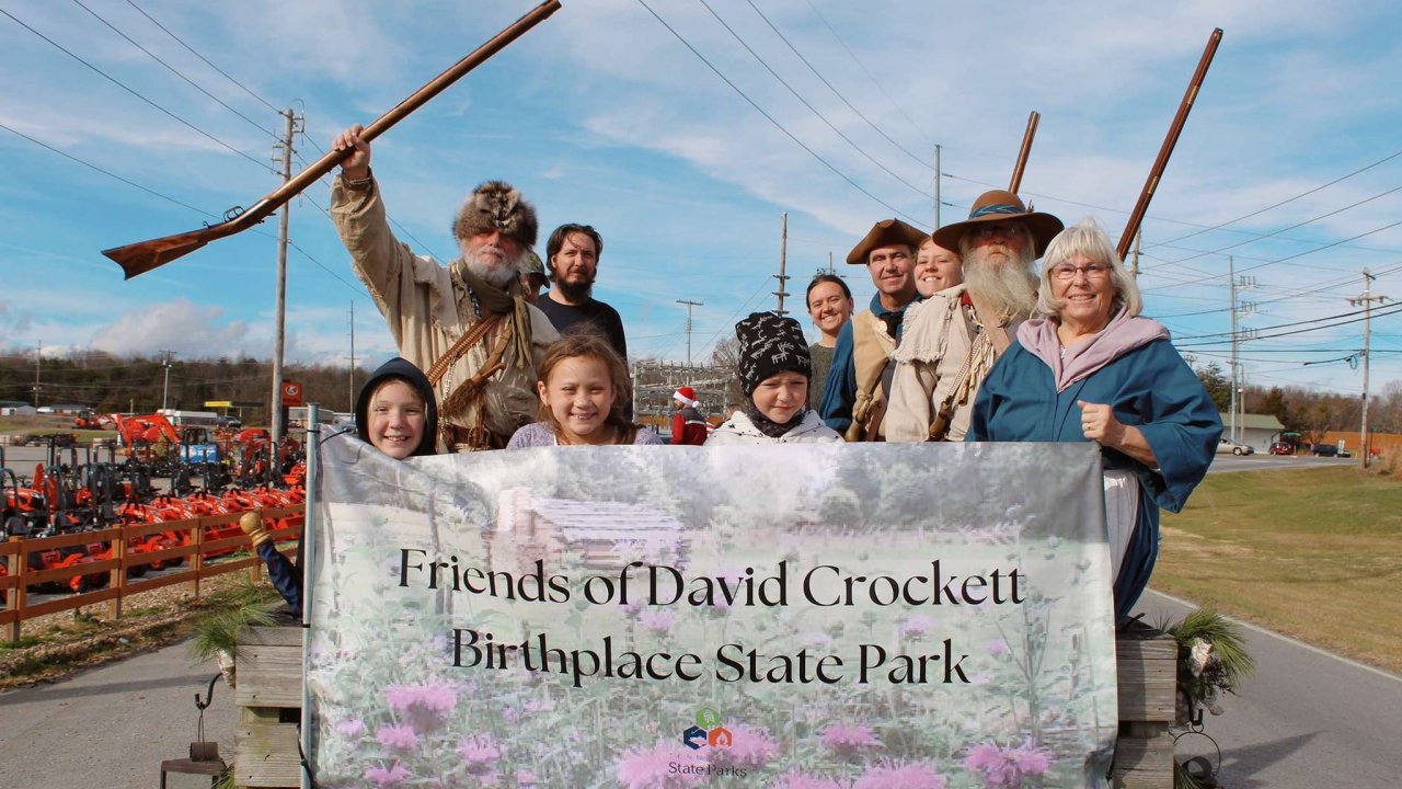 group of people posing behind a banner that says Friends of David Crockett Birthplace State Park