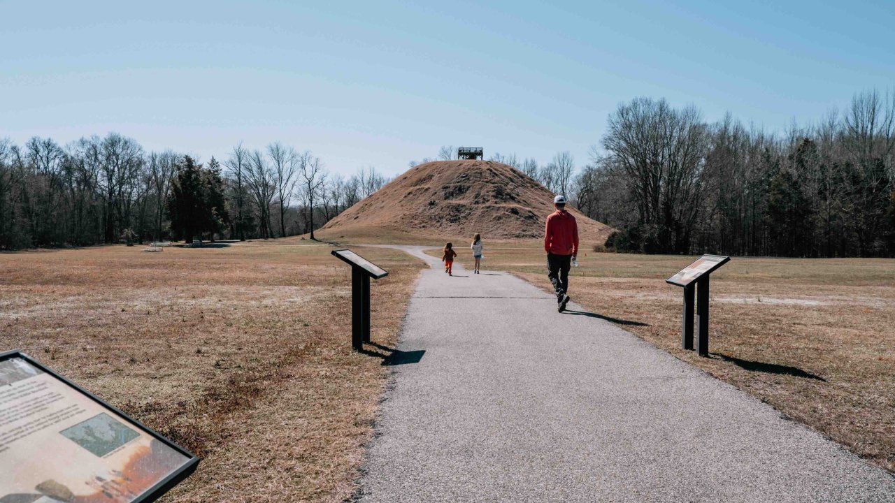 man and girl walking on a paved trail towards a mound passing information panels