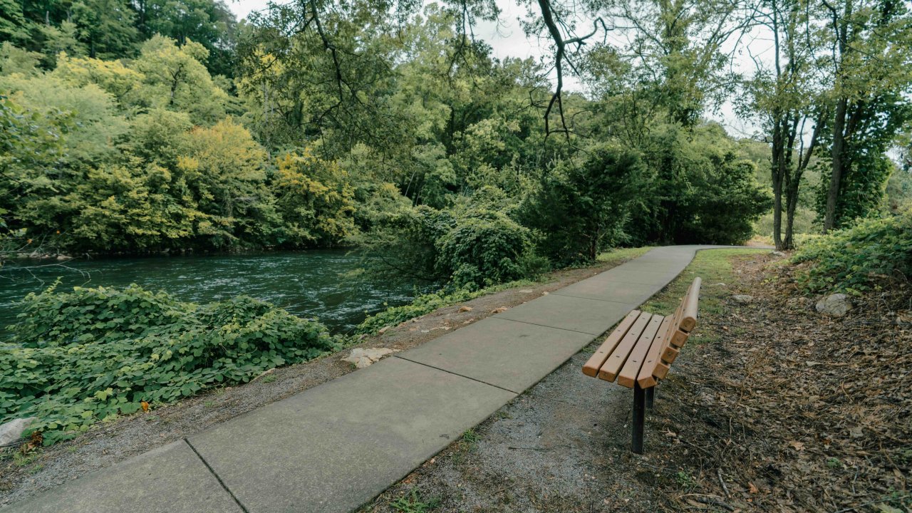 concrete trail that leads off to the right with a bench that faces toward the river