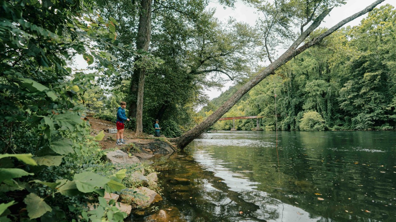 two people fishing in a calm river surrounded by trees