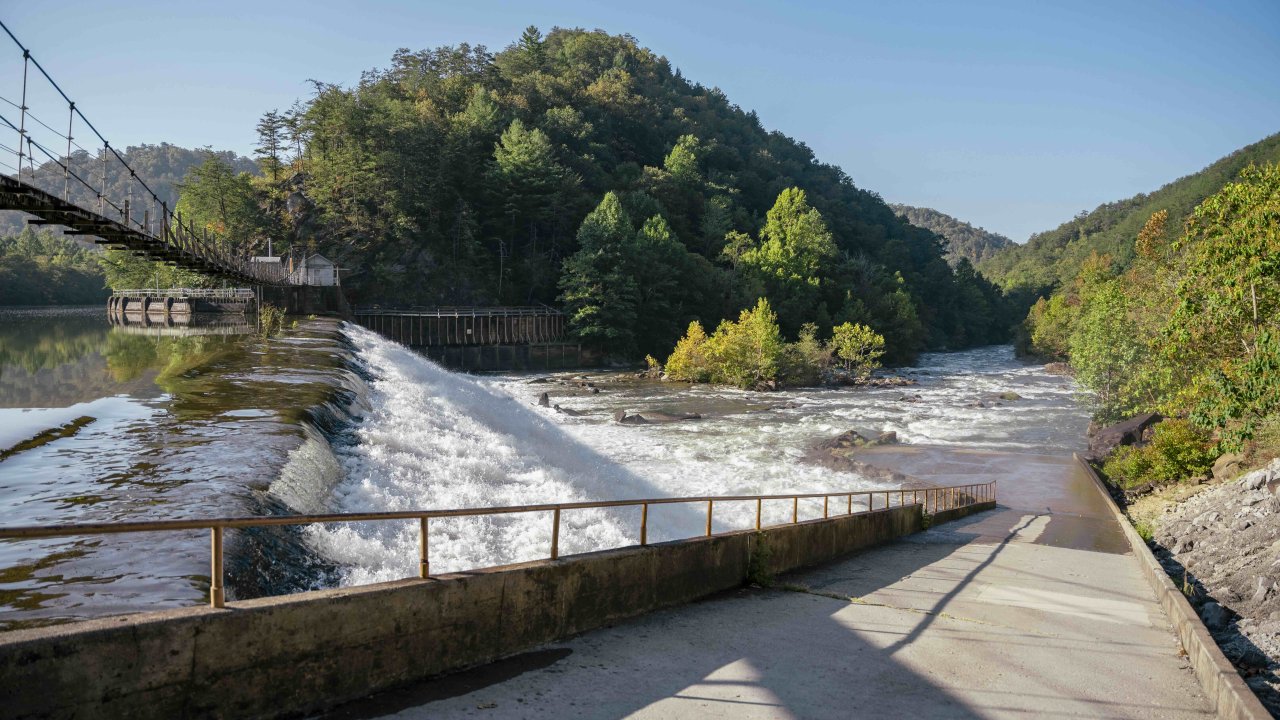 View of concrete slope for rafts, a narrow bridge, and of a river that has a small drop