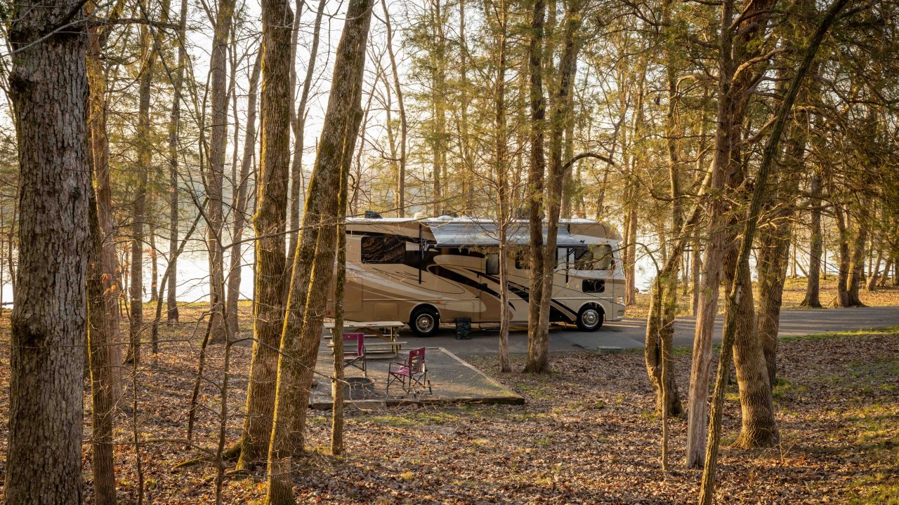 Motorhome parked in a forested area near a lake at sunset.