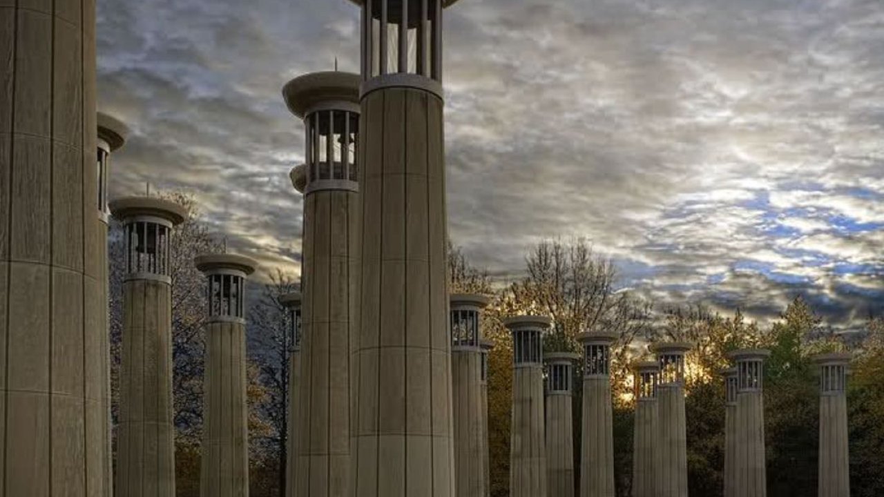 Tall, cylindrical stone columns in a park at sunset with dramatic clouds.