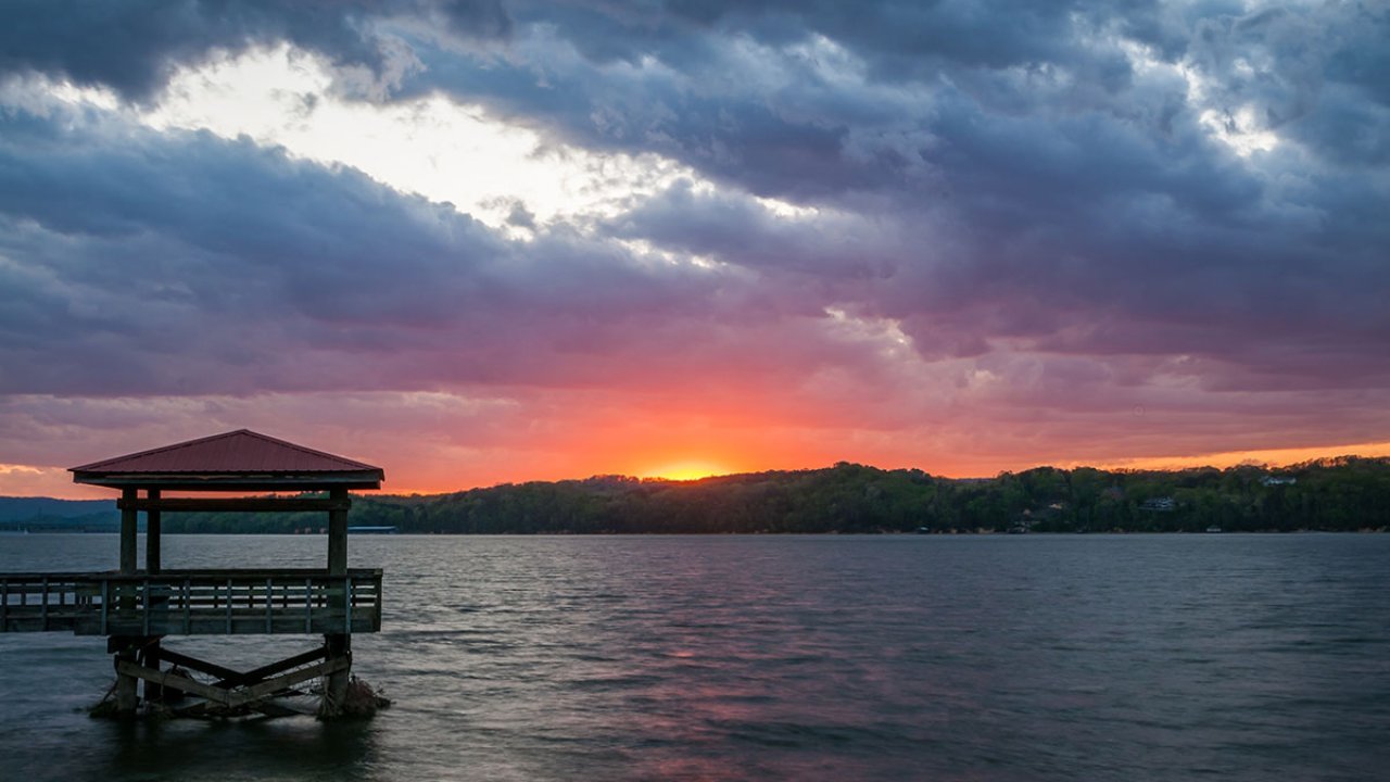Sunset over a lake with a silhouette of a gazebo on a pier.