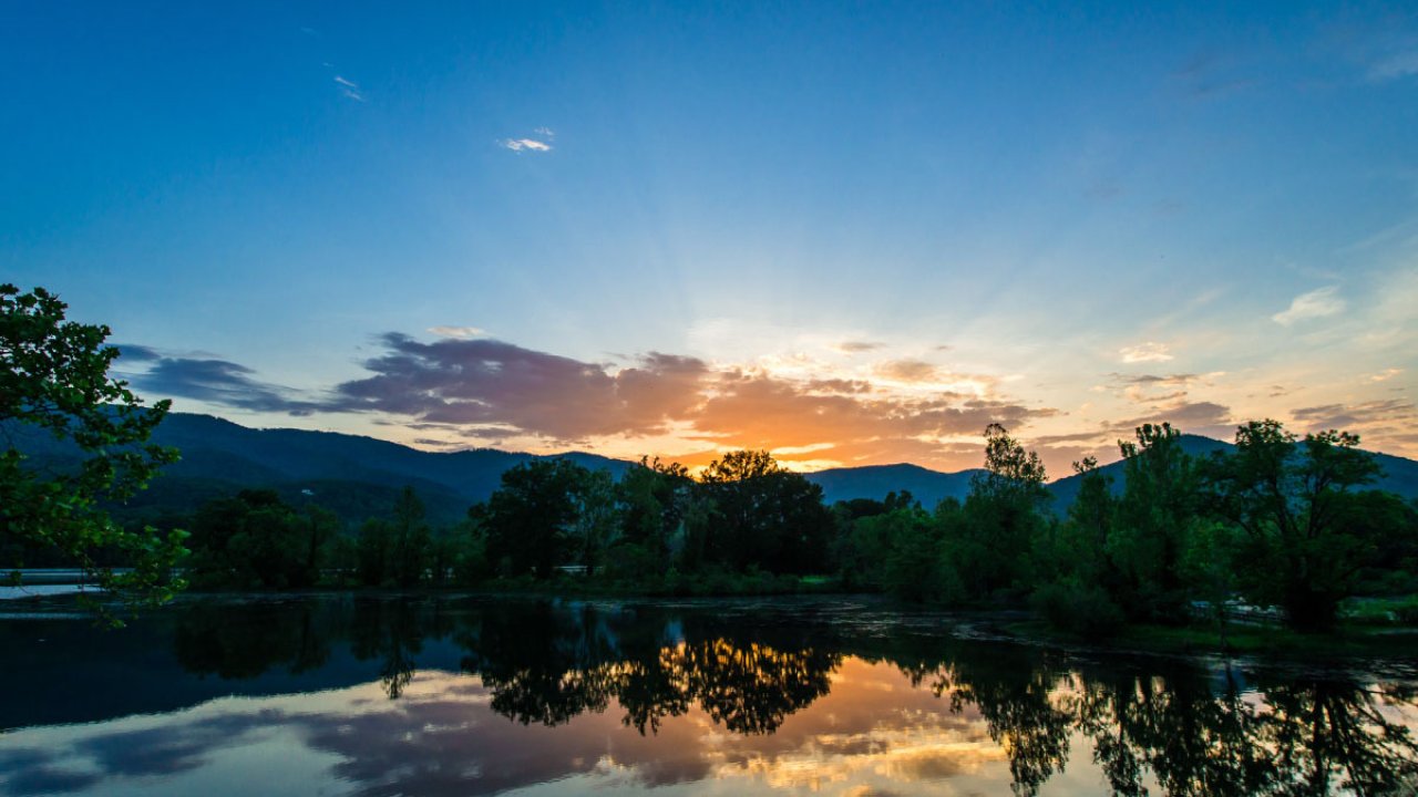 Sunset over a calm lake with reflected clouds and silhouetted mountains.