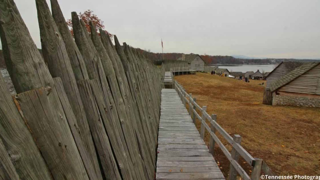 Wooden fence and walkway leading through a historic village on a cloudy day.