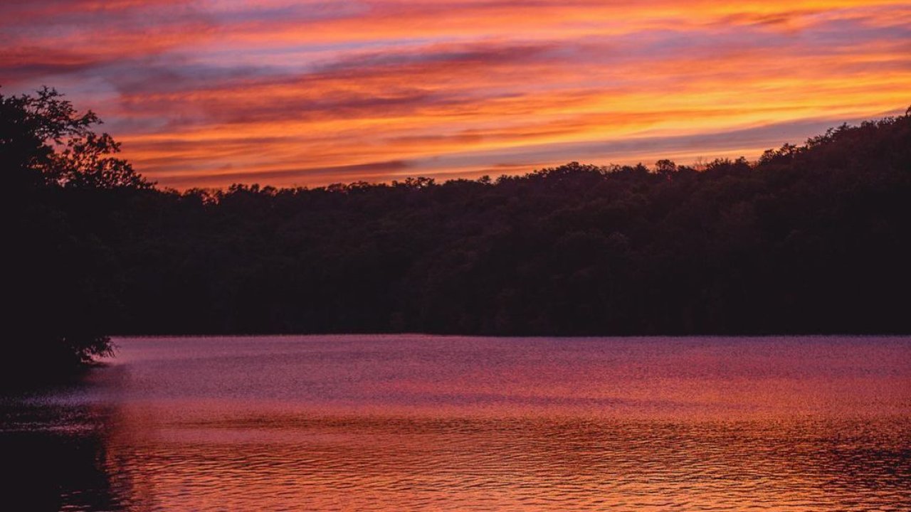 Vivid sunset over a tranquil lake with orange and purple skies.