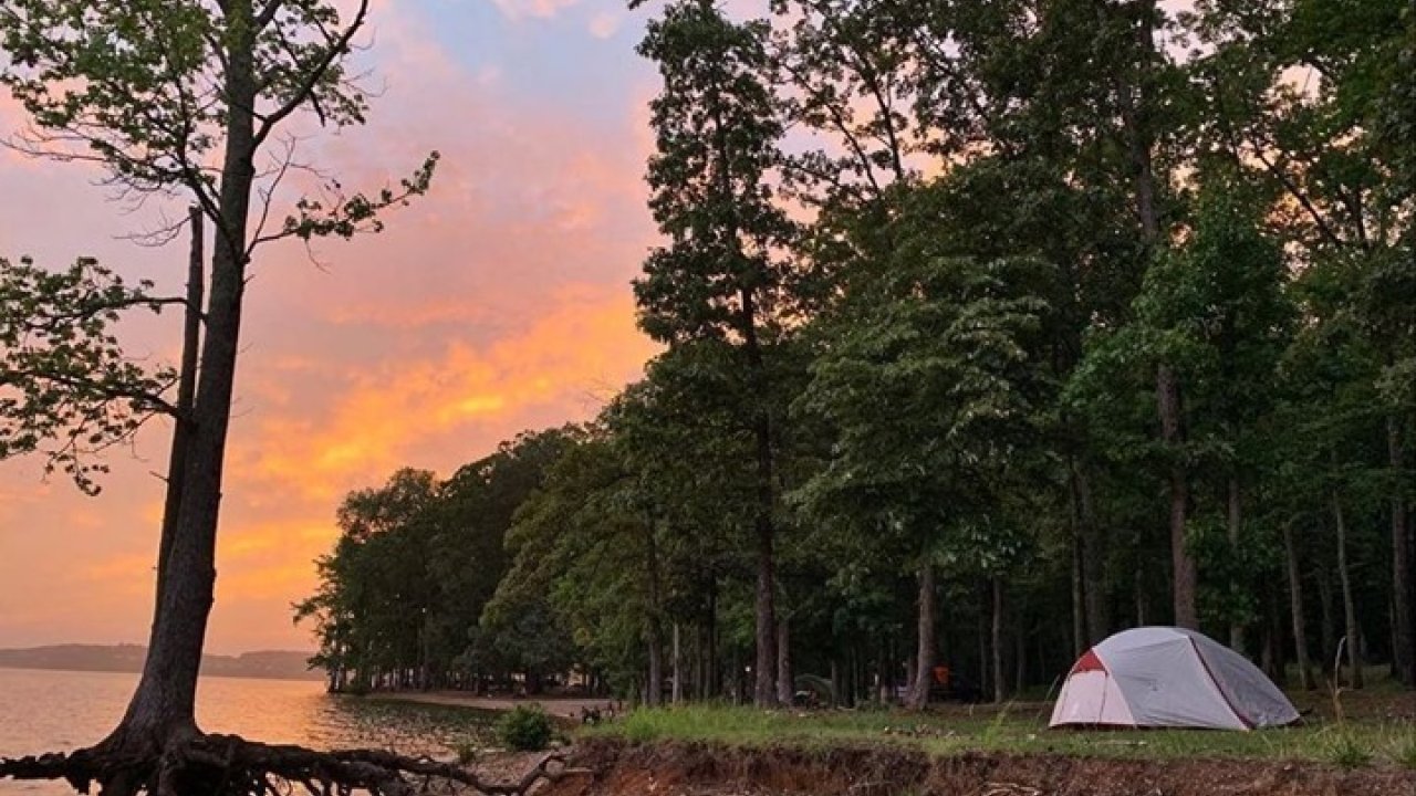 Sunset at lakeside campsite with a tent under colorful sky.