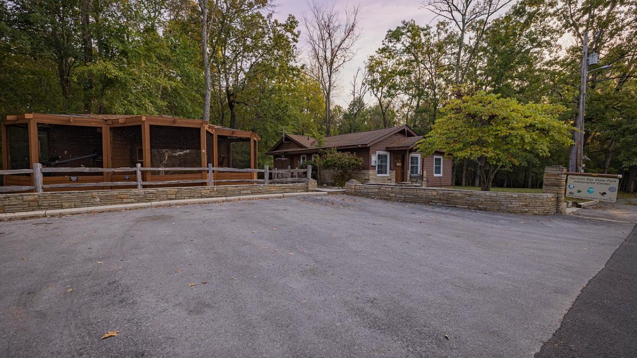 Gravel parking lot in front of a cabin and covered area surrounded by autumn trees.