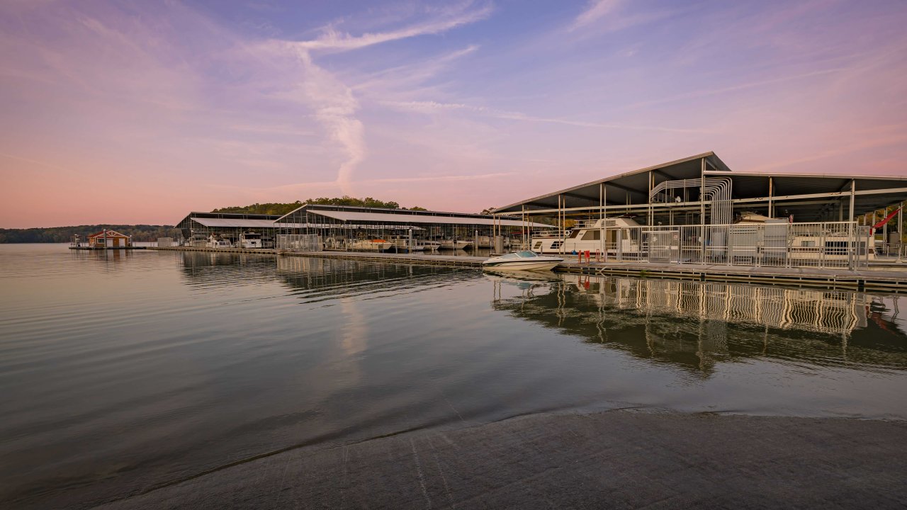 Sunset over a serene lake with a modern waterfront building reflected in the water.