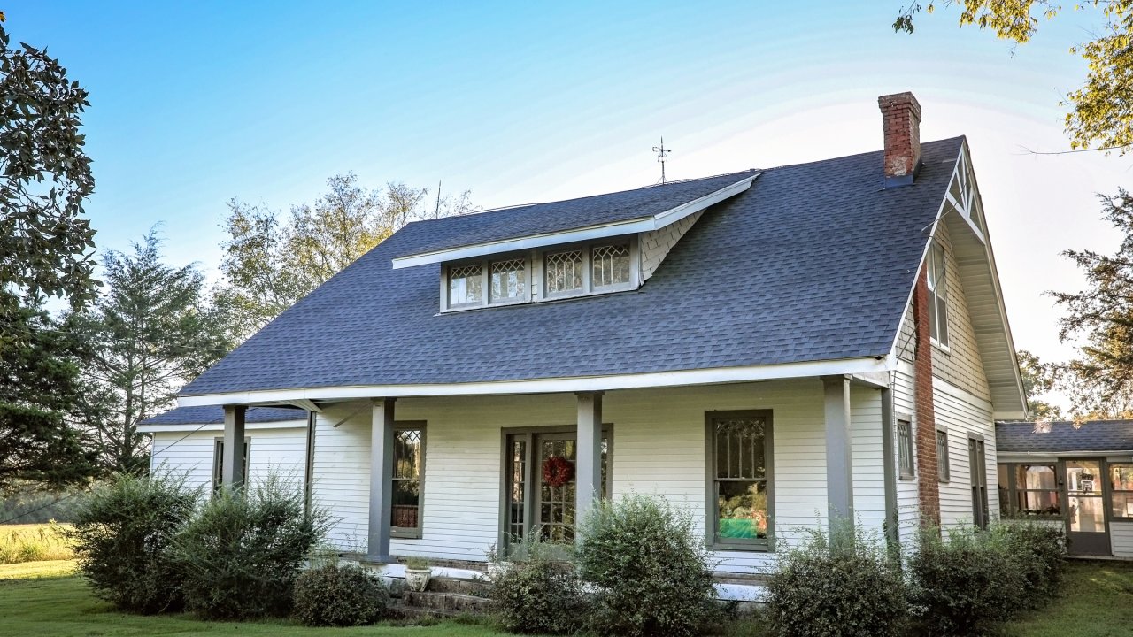 White cottage with a gable roof and front porch, surrounded by green shrubs.