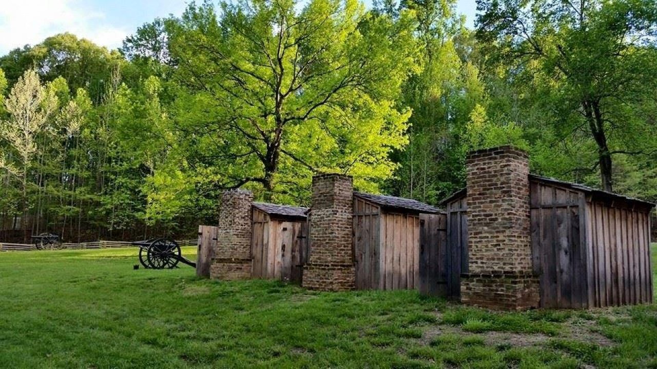 Rustic wooden cabins with stone chimneys in a lush green forest setting.