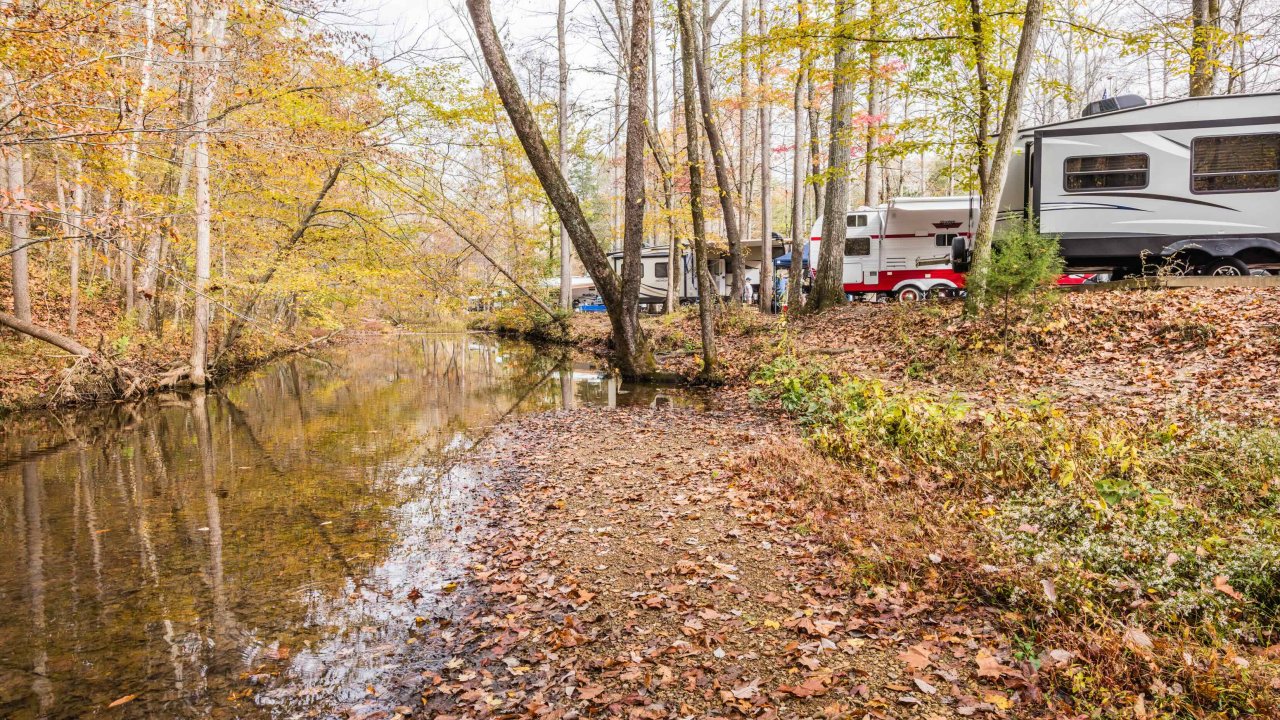 Autumn campground scene with RVs beside a reflective creek.