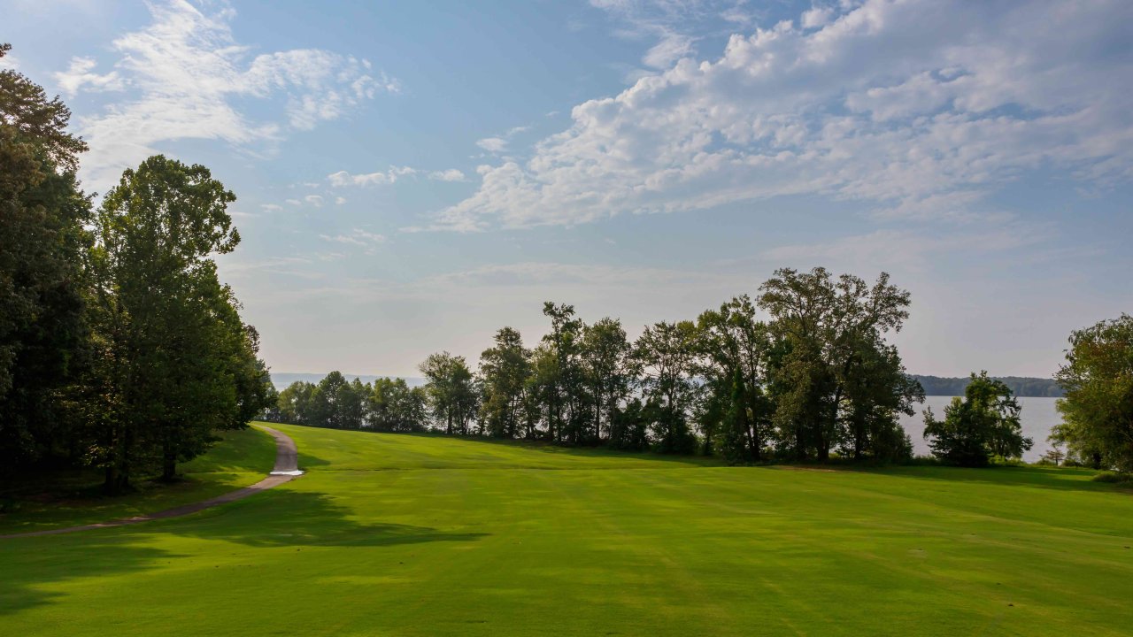 Lush golf course with a curving path near a lake under a clear sky.