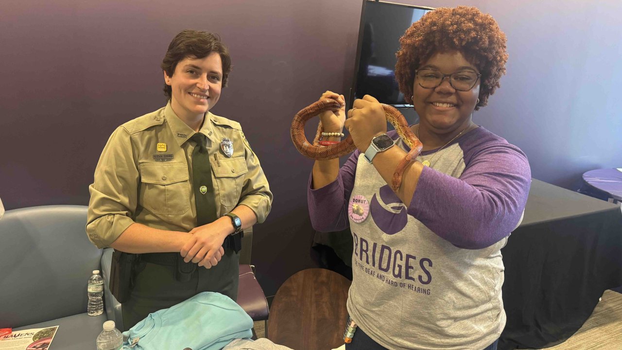 Two women smiling, one holding a snake at an educational event.