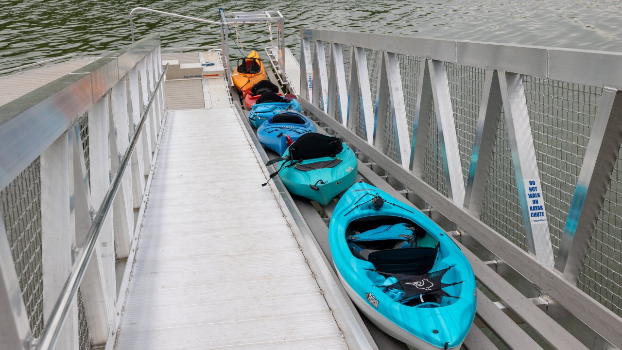 Four colorful kayaks lined up on a metal dock by the water.