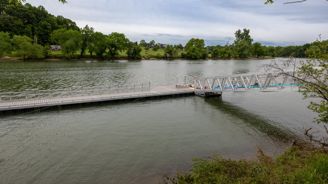Calm river with a floating dock, surrounded by trees and greenery.