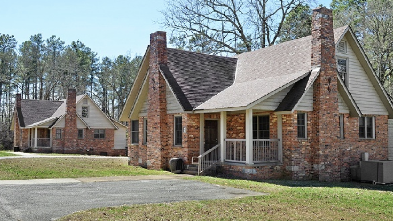 A brick lodge cabin stands next to a similar one in a large green field. 