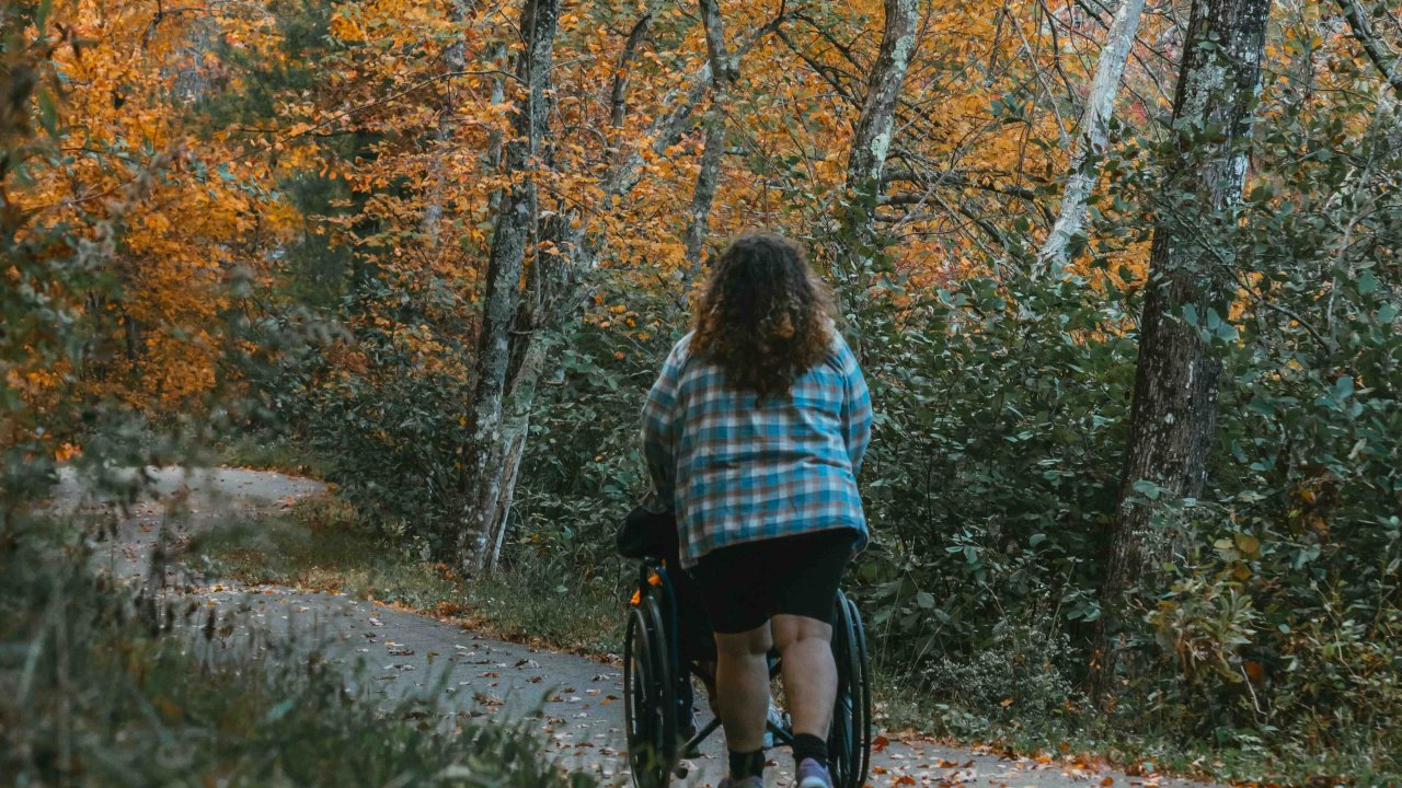 Woman walking with a bicycle on a path surrounded by autumn trees.