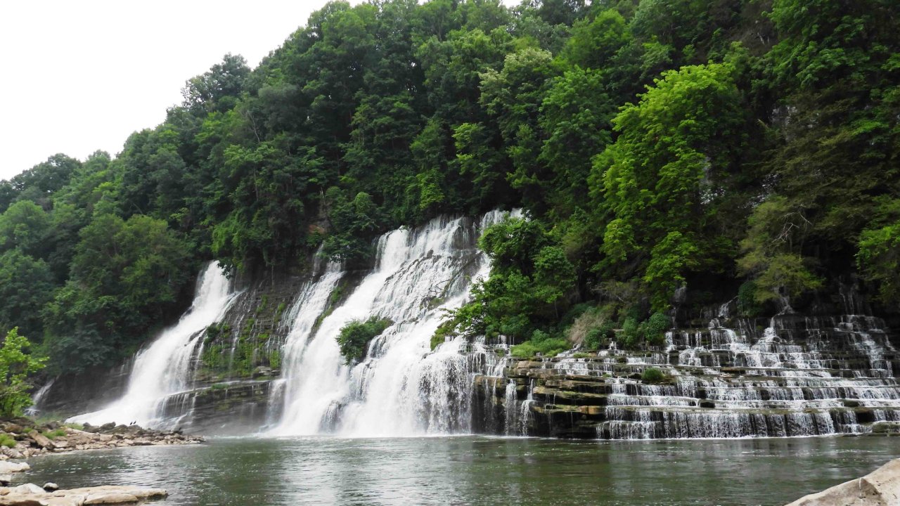 Scenic waterfall cascading into a serene river surrounded by lush greenery.
