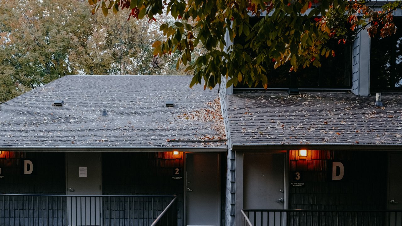 Autumn leaves frame a two-story building with glowing porch lights.