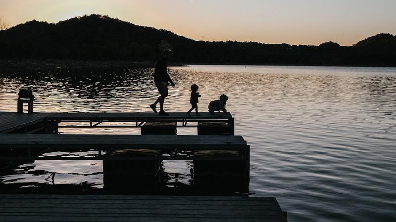 Silhouette of a person and two children on a dock at sunset.
