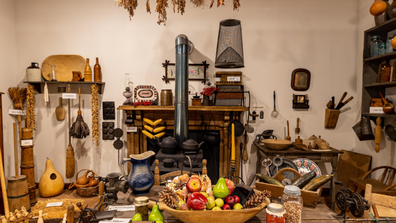Historical kitchen display with vintage utensils and fruit on a wooden table.