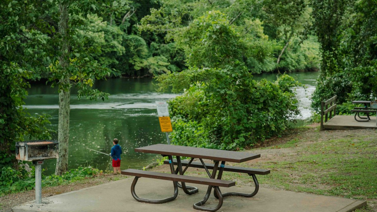 ADA accessible trail leading to a picnic table next to a grill and a river.
