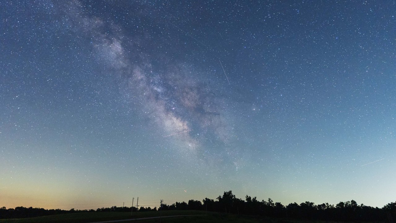 starry night sky making a line in the sky with trees in the distance