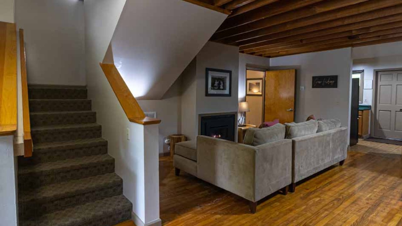 Cozy living room with staircase, wooden ceiling beams, and hardwood floors.