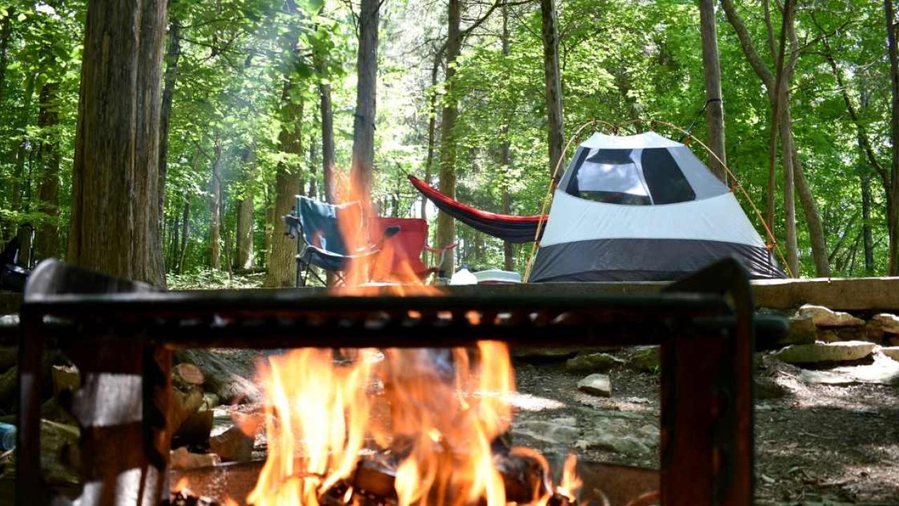 campsite with a campfire, a tent, and chairs.