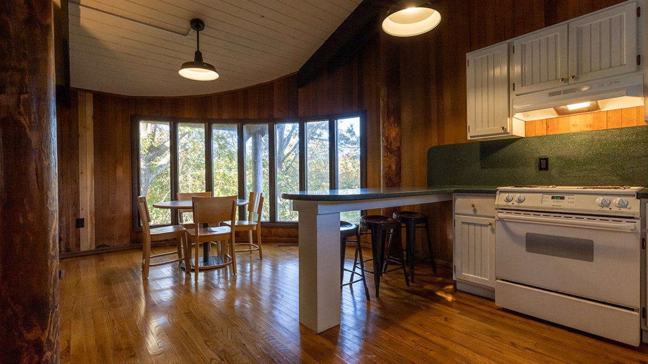 Cozy kitchen with hardwood floors, white cabinets, and forest view through large windows.