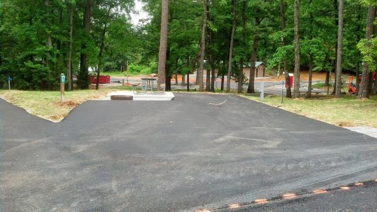 Newly paved road in a park with green trees and buildings in the background.
