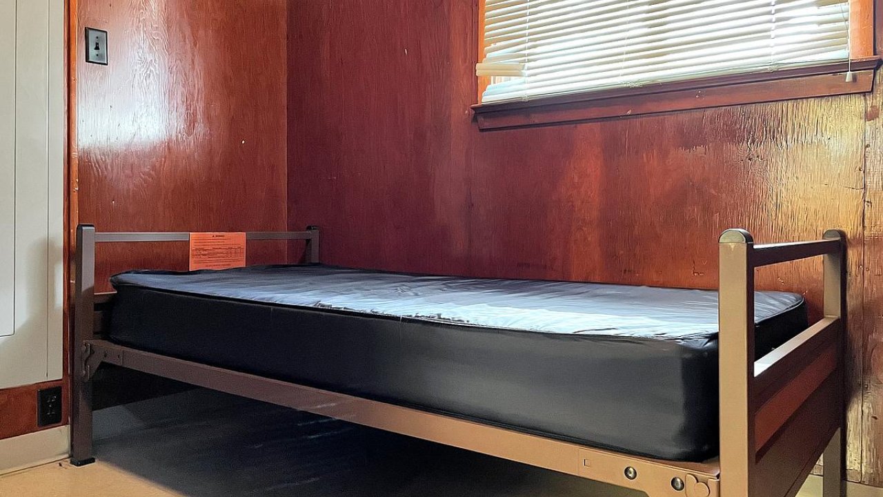 Single bed with black mattress in a room with wooden walls and a window.