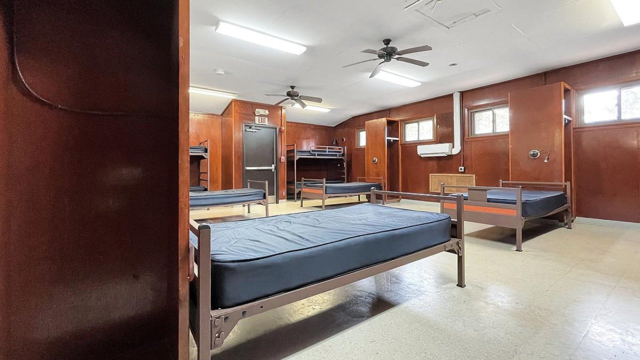 Empty dormitory room with two bunk beds and wooden paneling.