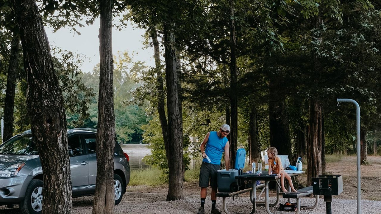 Family picnic at a forest campsite with an SUV nearby.