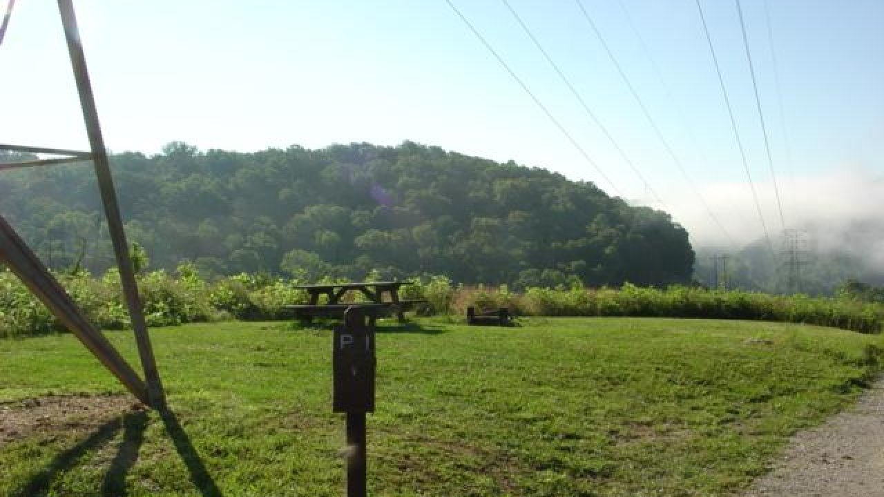 Green field with picnic table, mist over distant hills, sunny sky.