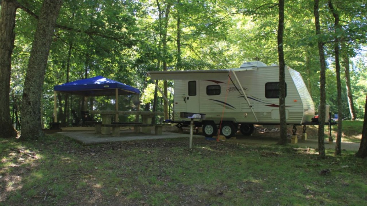 Camper trailer parked in a wooded campsite under green trees.