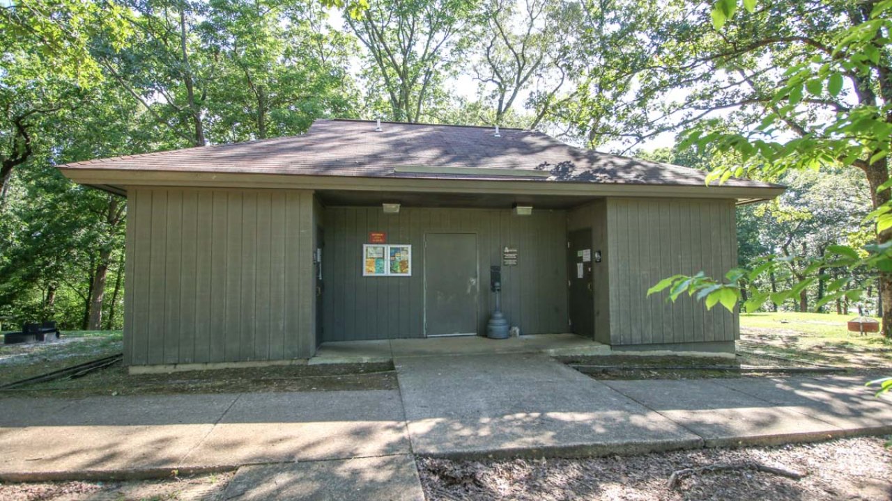 Gray restroom building surrounded by trees in a park setting.