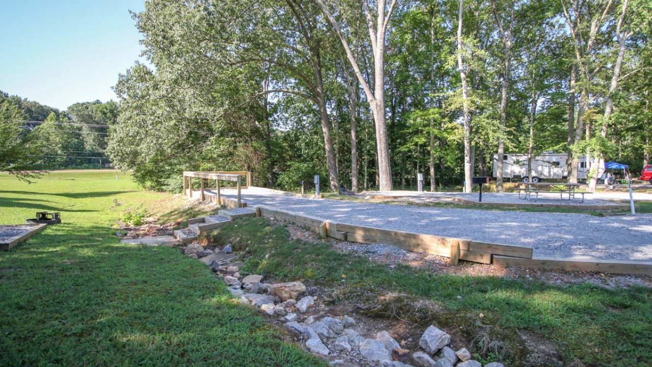 Campground site with trees and a gravel driveway.