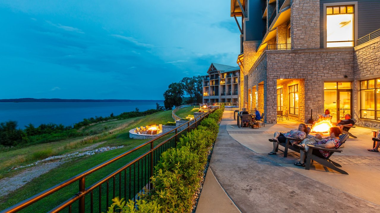 People enjoying evening at lakeside fire pits outside a modern building.