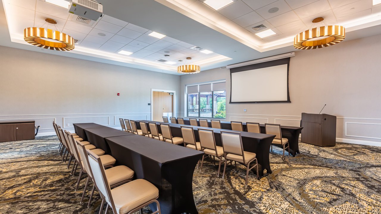 Empty conference room with rows of chairs, a projector, and a screen.