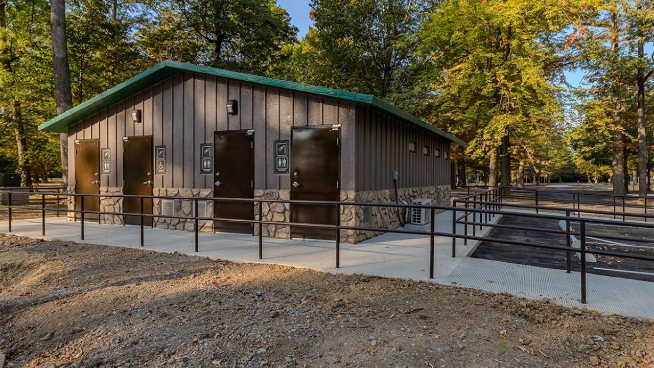 Restroom building in a wooded area, metal roof, surrounded by trees.