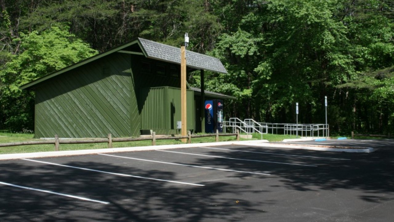 Green shed and vending machines by an empty parking lot, surrounded by trees.