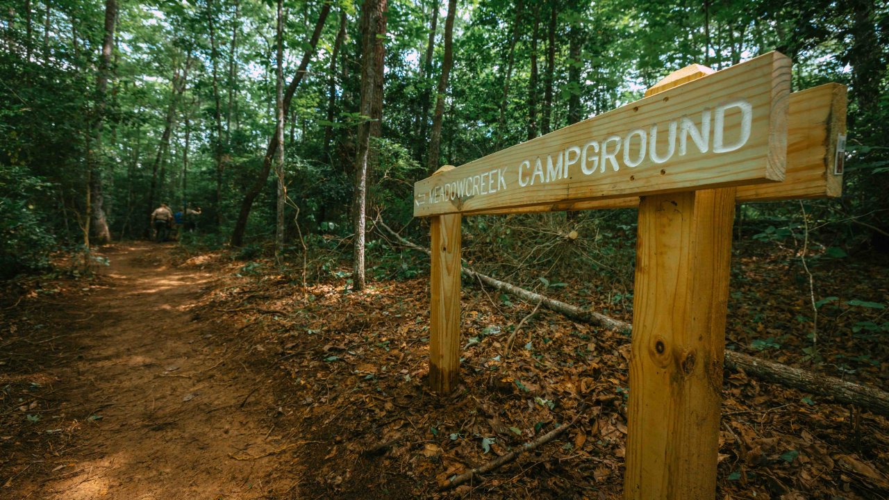 Forest trail with a wooden campground sign.