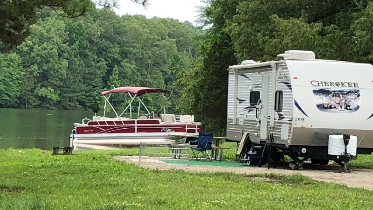 Pontoon boat next to an RV on a lush lakeside.