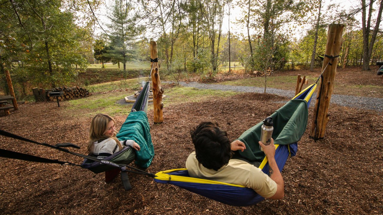 Father and child playing on a hammock in a forest playground.