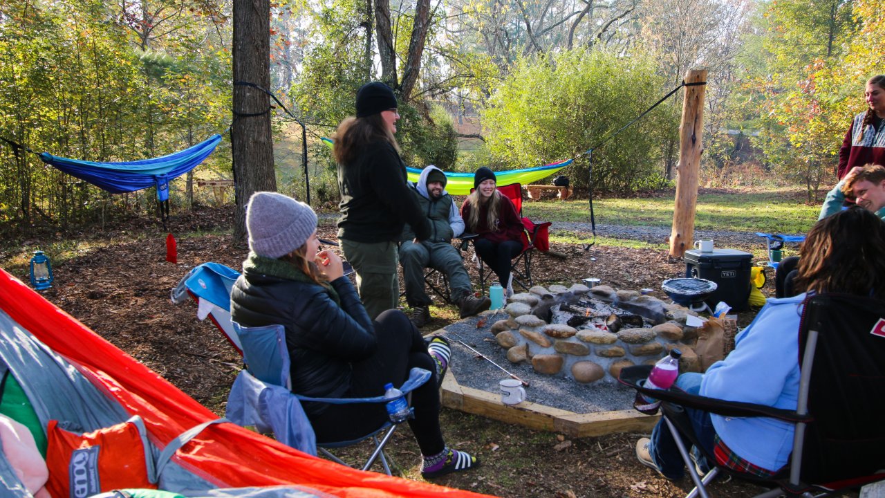 Group of friends enjoying a camping trip with a hammock and campfire.