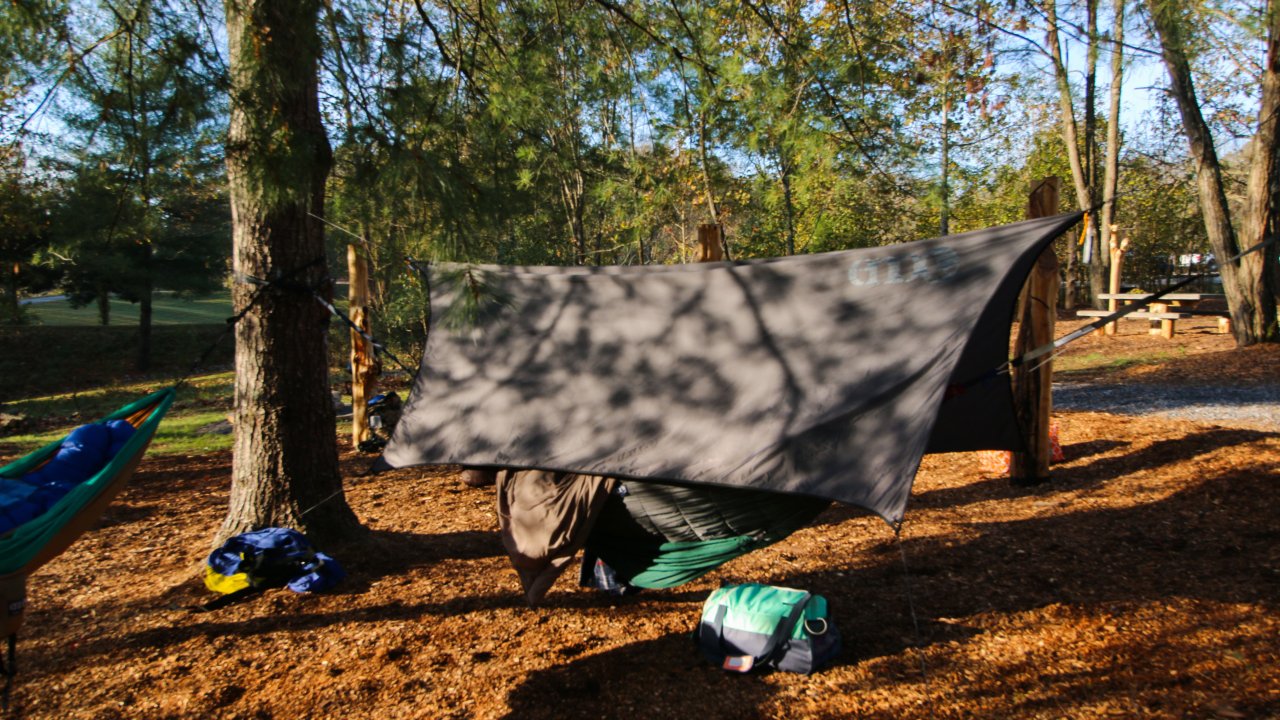 Tarp shelter and hammocks set up in a forest camping area.